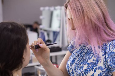 Profesyonel makyöz güzellik salonundaki güzel bayan modellere makyaj yapıyor..                   