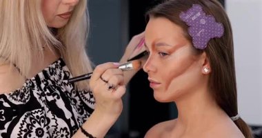 Profesyonel makyöz güzellik salonunda güzel bir genç kadın için makyaj yapıyor.                                   