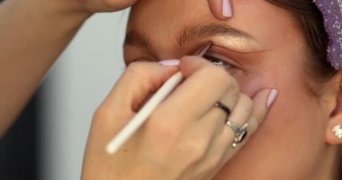 Güzellik salonunda genç ve güzel bir kadına göz makyajı yapan profesyonel bir makyöz.                         