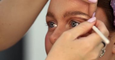 Güzellik salonunda genç ve güzel bir kadına göz makyajı yapan profesyonel bir makyöz.                         