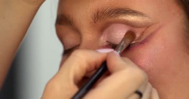 Güzellik salonunda genç ve güzel bir kadına göz makyajı yapan profesyonel bir makyöz.                         