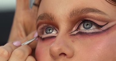 Güzellik salonunda genç ve güzel bir kadına göz makyajı yapan profesyonel bir makyöz.                         