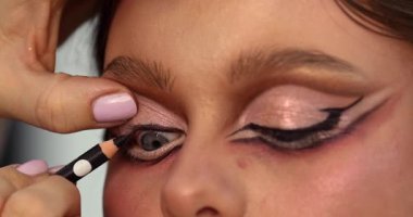 Güzellik salonunda genç ve güzel bir kadına göz makyajı yapan profesyonel bir makyöz.                         