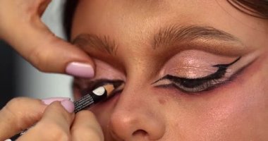 Güzellik salonunda genç ve güzel bir kadına göz makyajı yapan profesyonel bir makyöz.                         