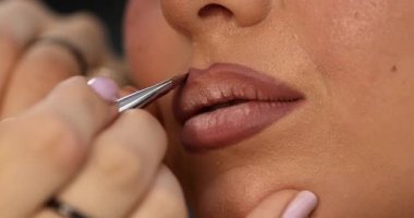 Profesyonel makyöz güzellik salonunda genç ve güzel bir bayana dudak makyajı yapıyor.                         