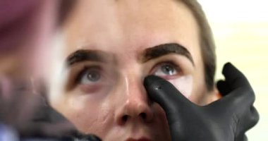 Güzellik salonunda genç bir kadına kirpik yapan profesyonel makyözün yakın plan görüntüsü.   