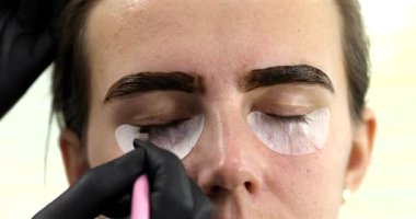 Güzellik salonunda genç bir kadına kirpik yapan profesyonel makyözün yakın plan görüntüsü.   