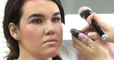 Stüdyoda makyajlı genç ve güzel bir kız. Makyaj sanatçısı güzellik salonuna kozmetik uyguluyor.                