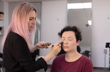 Profesyonel makyöz güzellik salonundaki güzel kadın mankene makyaj yapıyor..                      