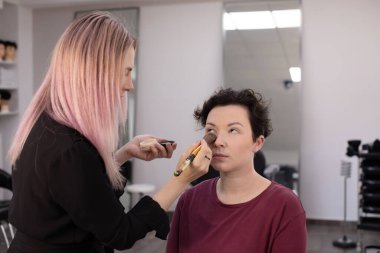 Profesyonel makyöz güzellik salonundaki güzel kadın mankene makyaj yapıyor..                      