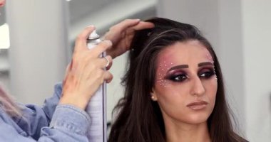 Profesyonel kuaför, güzellik salonunda mükemmel makyajlı genç ve güzel bir kadına şık saç stili yapıyor.                