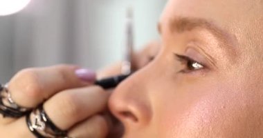 Makyaj sanatçısı güzellik salonundaki genç bir kadına makyaj yapıyor.       