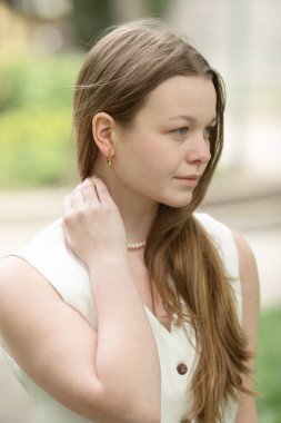 Parkta duran beyaz yelekli güzel, gülümseyen genç bir kadının portresi.                             