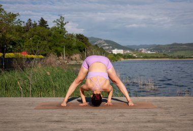 Odaklanmış genç bayan gölün kenarında yoga pozu veriyor.                           