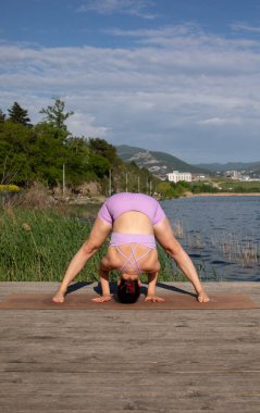 Odaklanmış genç bayan gölün kenarında yoga pozu veriyor.                           