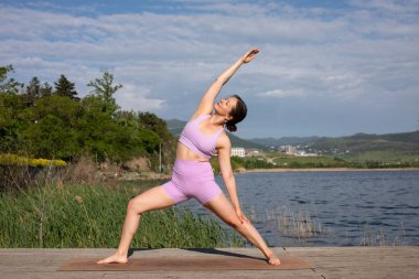Odaklanmış genç bayan gölün kenarında yoga pozu veriyor.                           