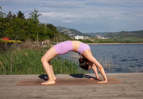 Odaklanmış genç bayan gölün kenarında yoga pozu veriyor.                           