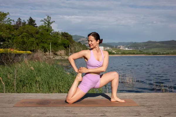 Odaklanmış genç bayan gölün kenarında yoga pozu veriyor.                           