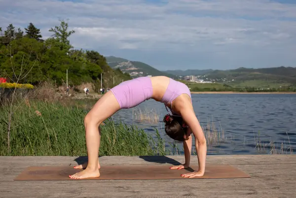 Odaklanmış genç bayan gölün kenarında yoga pozu veriyor.                           