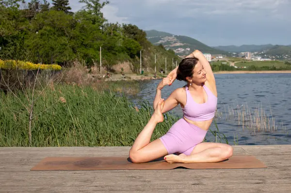 Odaklanmış genç bayan gölün kenarında yoga pozu veriyor.                           