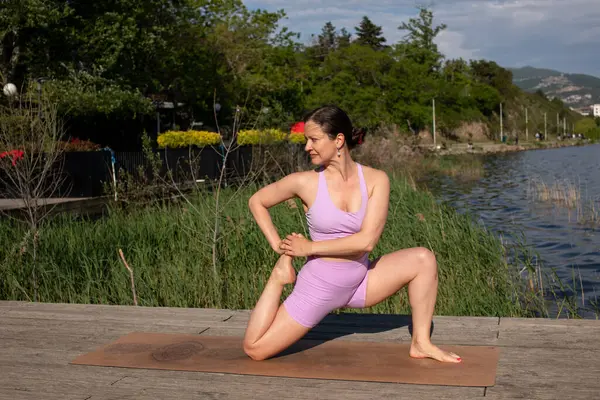 Odaklanmış genç bayan gölün kenarında yoga pozu veriyor.                           