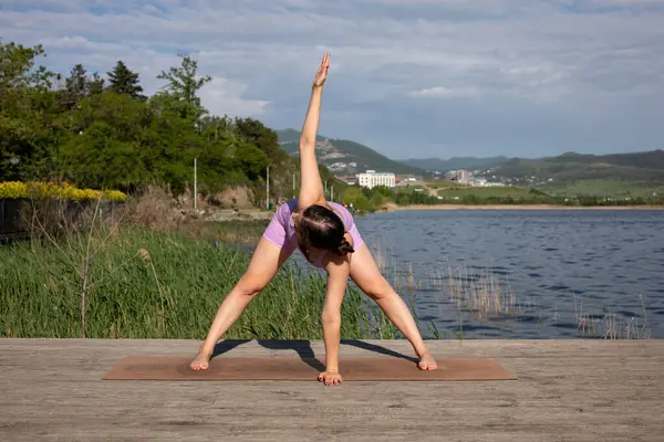 Odaklanmış genç bayan gölün kenarında yoga pozu veriyor.                           