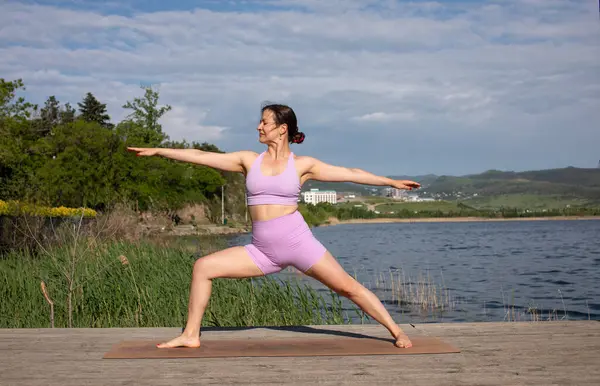 Odaklanmış genç bayan gölün kenarında yoga pozu veriyor.                           