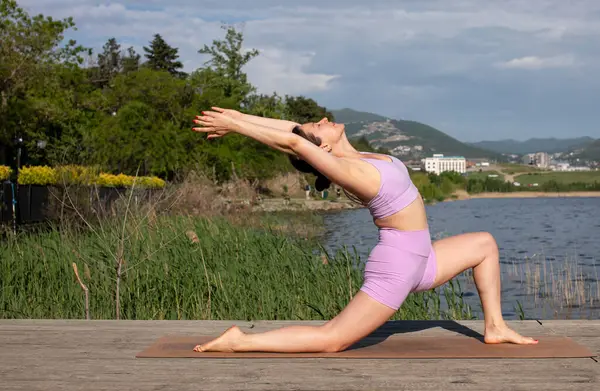 Odaklanmış genç bayan gölün kenarında yoga pozu veriyor.                           