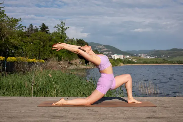 Odaklanmış genç bayan gölün kenarında yoga pozu veriyor.                           