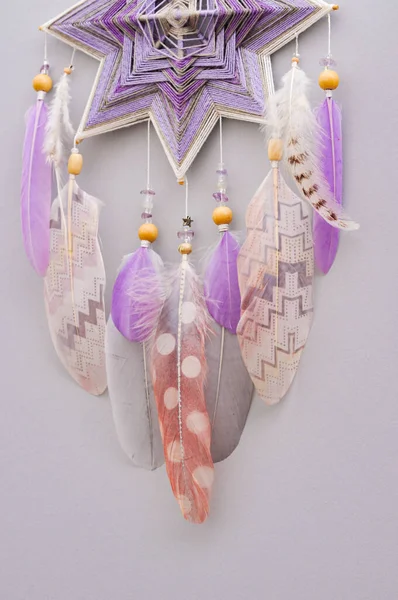 灰色の背景に羽とアメジストの宝石を持つ手作りの密教織りマンダラ魔法の夢のキャッチャー ヨガルームインテリアのための瞑想ツール ロイヤリティフリーのストック画像