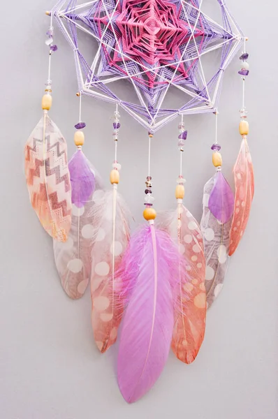 灰色の背景に羽とアメジストの宝石を持つ手作りの密教織りマンダラ魔法の夢のキャッチャー ヨガルームインテリアのための瞑想ツール ストックフォト