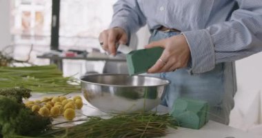 female doing new bouquet. Girl working in flower shop studio. Female florist artist cleans flowers for a beautiful bouquet, workplace view. High quality 4k footage