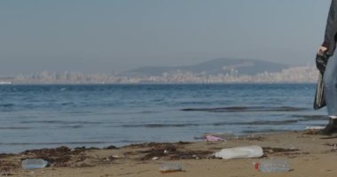 eco-activist girl collects plastic trash on the coast. Young woman collects plastic garbage in a garbage bag on the sandy beach of the sea. Girl cleans ocean coastline from plastic bottle trash on