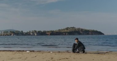 eco-activist girl collects plastic trash on the coast. Young woman collects plastic garbage in a garbage bag on the sandy beach of the sea. Girl cleans ocean coastline from plastic bottle trash on