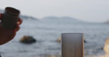 Uçurumun kenarındaki deniz kıyısına yürürken ocakta kahve yapan bir kadın. Yüksek kalite 4k görüntü