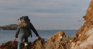 Uçurumun kenarında sırt çantalı bir kadın şehre bakıyor. Gezgin dağda duruyor. Deniz kenarındaki dağlarda yürüyüş. Yüksek kalite 4k görüntü