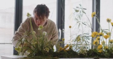 female doing new bouquet. Florist makes a floral oasis. Girl working in flower shop studio. Female florist artist cleans flowers for a beautiful bouquet, workplace view. High quality 4k footage