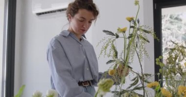 female doing new bouquet. Girl working in flower shop studio. Female florist artist cleans flowers for a beautiful bouquet, workplace view. High quality 4k footage