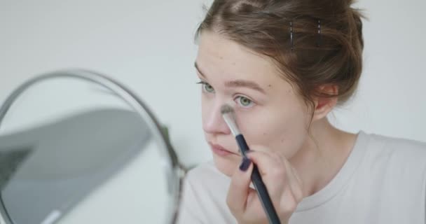 若い女性が彼女のまぶたを描き 鏡の中に自分自身を見ています 顔の女性の肌のケア 女の子のための化粧 美しい少女が目をペイントする 高品質4K映像 — ストック動画