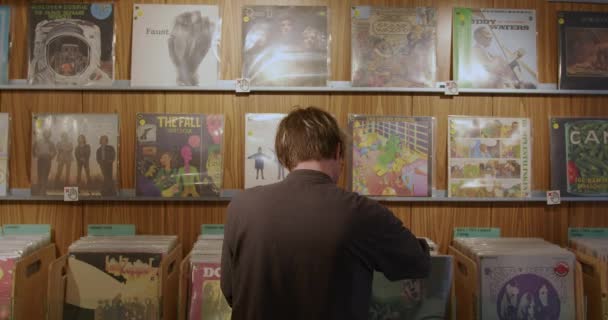 一个时髦的嬉皮士男人选择在音乐商店里的乙烯唱片作为音乐收藏品的礼物 Dj为派对买音乐 一个时髦的家伙正在一家古董店里用乙烯唱片寻找音乐 — 图库视频影像