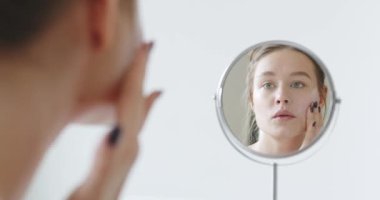 Genç bir kadın yüz derisine bakar. Güzellik tedavisi yapıyorum. Yüzüne krem sürüyorum. Sabah rutini. Güzellik, Şımartma, Kaplıca Konsepti. Cilt Bakımı Kozmetik Konsepti Yavaş