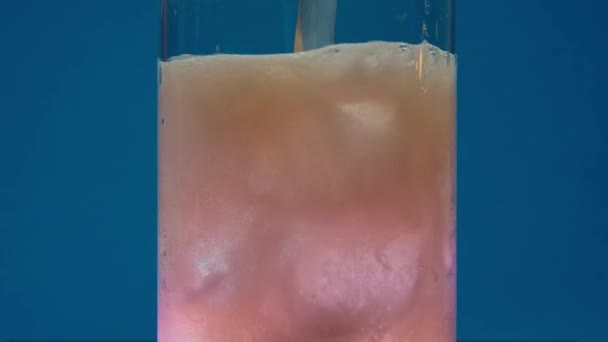 空の透明ガラスに落ちるアイスキューブのスローモーションクローズアップ ジューシーなオレンジ色の炭酸飲料は氷でガラスに注がれます スローモーションマクロ 背景ブルー バービーコア バービー — ストック動画