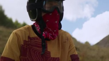 Engebeli bir motosikletçi koruyucu maskesini ve bandanasını başarıyla çıkardı. Yüzü yoğun bir off-road motorsiklet seferi sonrasında, yorgunluk ve memnuniyet ile kızardı.