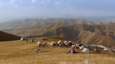 Kamp, görkemli dağ panoramasına karşı canlandıkça sabah oluyor. Çadırlar engebeli araziye dikkatlice kurulmuş. Canlı renkleri engebeli toprakla çelişiyor.