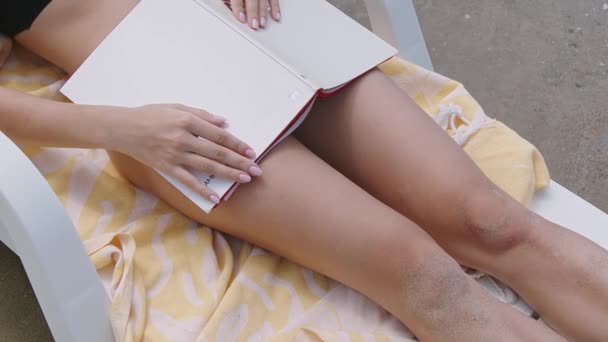 在海滩上一个女孩躺在海滩上看书 绿松石在后面摇曳 夏天的寒冷 在海上度假 休息和快乐 在海滩度假 高质量4K — 图库视频影像