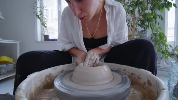 彼女が情熱的に粘土を陶器の車輪の将来の粘土花瓶の絶妙な形に形成するように若く熟練した陶磁器の芸術家 彼女の手は粘土に浸され 巧みに彼女の芸術的なビジョンをもたらします — ストック動画