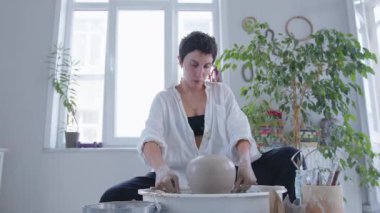 Seramik sanatçısı bir kız çömlekçi çarkında vazo yapıyor. Kadın sanatçılar yaratıyor, başarıyor, feminizm iş başında. Omzunun arkasından ellerle çalışmanın güzelliğine bak. Yavaşça yaklaş.