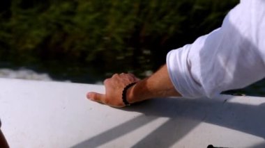 Bir adamın eli bir sürat teknesinin yatında dinleniyor. Dalgalar ve köpükler bırakarak hızla süzülüyorlar. Nehirde bir motorlu tekne gezisi. Zengin insanların geri kalanı. Beyaz gömlekli bir beyefendi seyahat ediyor.