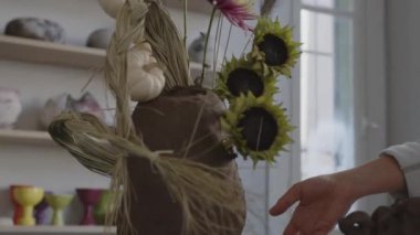 Yetenekli bir kadın sanatçı olarak, sanatının dağınık araç ve materyalleri ile çevrelenmiş yaratıcı ifade dünyasına adım atmak, kilden bir vazoda alışılmadık bir buketi canlandırır. Bunun içinde