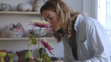 Yetenekli bir kadın seramikçi parlak bir atölyede sihrini gösterirken sanatsal yaratılış sürecine tanık olun. Dağınık malzeme ve aletlerle süslenmiş bir masanın önüne yerleştirilmişti.